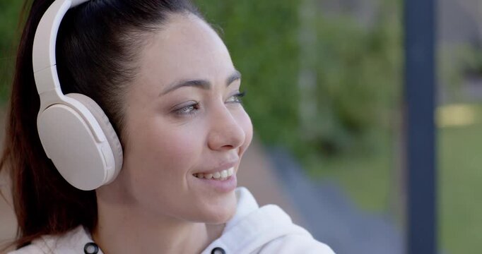 Woman in white hoodie, white headphones turning head on porch, responding to audio and smiling