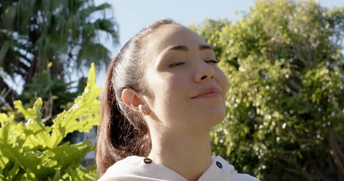 Woman closing eyes, tilting head into sunlight in backyard, wearing light hoodie, feeling sun