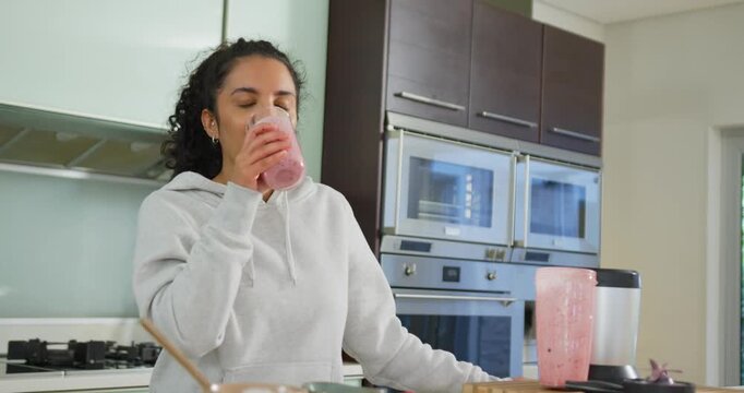 African American woman lifting glass after blending, closing eyes tasting pink smoothie at counter