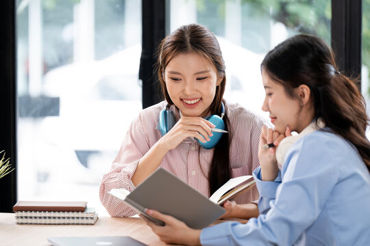 Two happy Asian students or coworkers studying together with books and headphones.