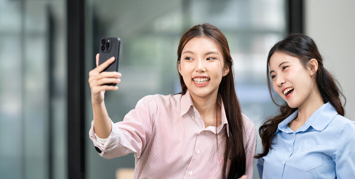 Two happy Asian women taking a selfie or making a video call on a smartphone.