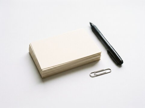 Stack of blank cream colored index cards with a black pen and paperclip on a clean white background for study and organization