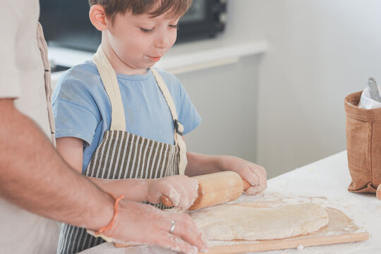 A young mother, father and son stretch and pull the bread dough in a bright modern kitchen, celebrating home life and family connection, a cosy lifestyle moment of love and belonging.