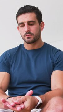 Vertical video: Looking down man in navy tee and light shorts rubbing palms, tapping watch and band
