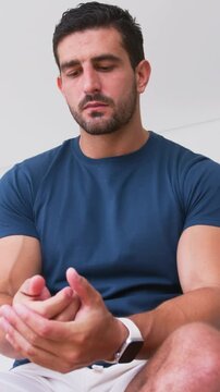 Vertical video: Looking down man rubbing hands, rolling wrists at home thinking with watch navy tee