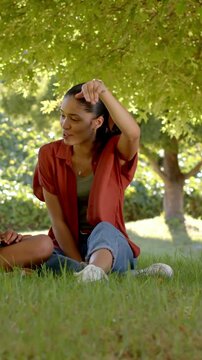Vertical video: Waving woman in rust shirt gesturing while responding to companion in park, watch