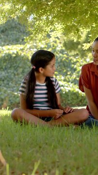 Vertical video: Listening child in striped tee studying small item on grass while adult speaking