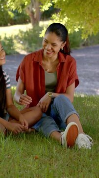 Vertical video: Laughing mother in rust shirt shifting gaze, reaching, comforting daughter at park