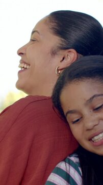 Vertical video: Laughing mom and daughter leaning on porch after joke in rust top with hoop earring