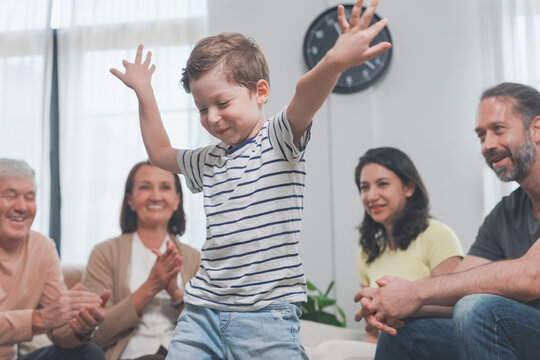 Three generations of one family cheer and clap with the little boy on a cosy couch at home, celebrating home life and family connection, a cosy lifestyle moment of love and belonging.