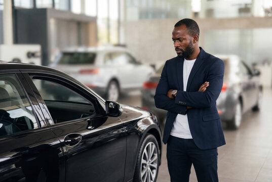 Serious man in suit examining black car at dealership