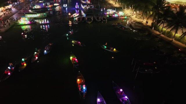 Illuminated boats move gracefully along the river in Hoi An, Vietnam, showcasing a lively atmosphere filled with colorful lights and reflections