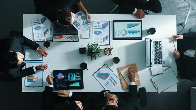 Top down aerial view of skilled businessman pointing financial chart at whiteboard while smart investor listening presentation and analyze stock market investment graph at meeting table. Directorate.