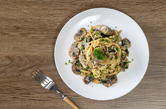 Spaghetti with champignon mushrooms and cream cheese on a wooden table