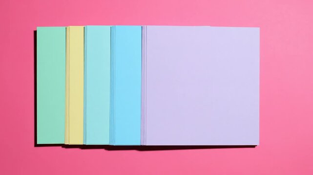 Hand touching pastel colored paper sheets with soft pink nail polish on bright pink background