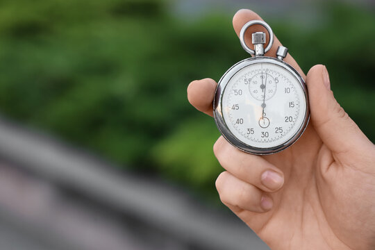 Hand holding a classic analog stopwatch with a white face and chrome casing against a blurred green background