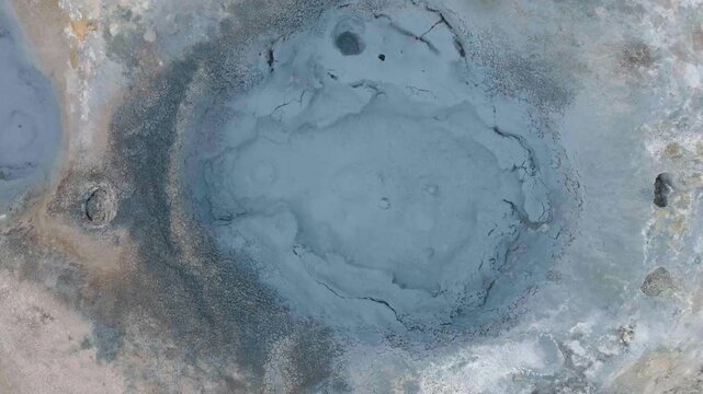 Aerial view of a bubbling mud pot in a geothermal area, steaming and abstract patterns on hot volcanic earth.