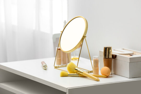 Different cosmetics and mirror on dressing table near white wall in room