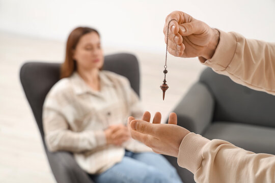 Male psychologists hands with pendulum hypnotizing woman in office, closeup