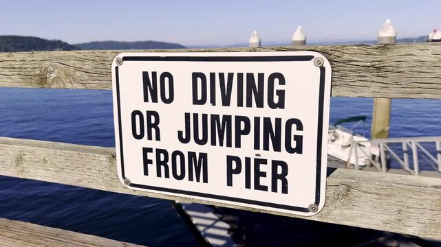 Warning sign prohibits diving or jumping from a pier above the water. Safety notice for waterfront public space and recreation area.