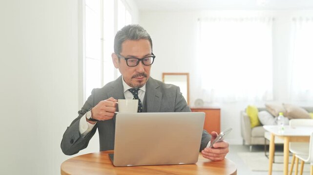 スマホとノートPCを見るミドル男性。DX、カフェ、アプリ、ニュース、動画、リラックス、休憩、投資家