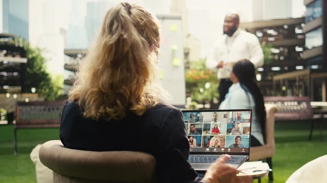 Employee using web conference virtual meeting for project planning, outdoor meeting with online presentation on laptop in business park.