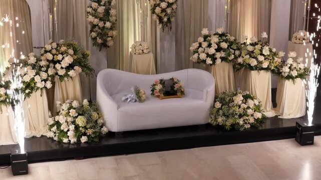 Drone shot approaching a luxurious bride and groom seating area decorated with white roses and candles.