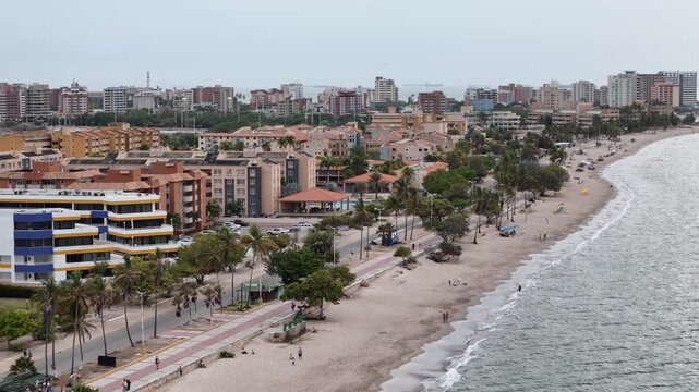 Drone view overlooking a sandy beachfront boulevard with apartment complexes and palm trees.