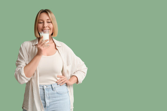 Beautiful young woman with glass of fresh milk on green background