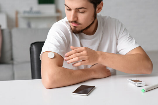 Diabetic young man with glucose sensor at home, closeup