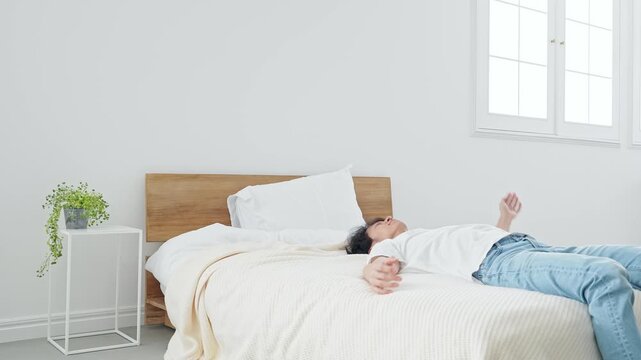 ベッドに寝転がる男性。寝不足、不眠症、あくび、寝坊、二度寝、ストレス、疲労、ダラダラ、昼寝、ベッド