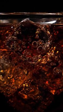 Fizzling cold beverage in the glass. Closeup on black background. Vertical footage