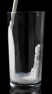 Pouring milk into the glass. Closeup on black background. Vertical footage