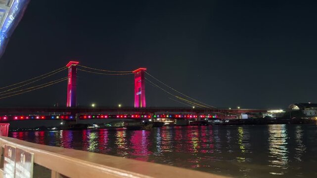 Ampera Bridge at night with colorful lights crossed by fishing boats in Palembang, Indonesia