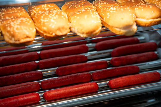 Close up of hot dogs and sesame buns on grill.