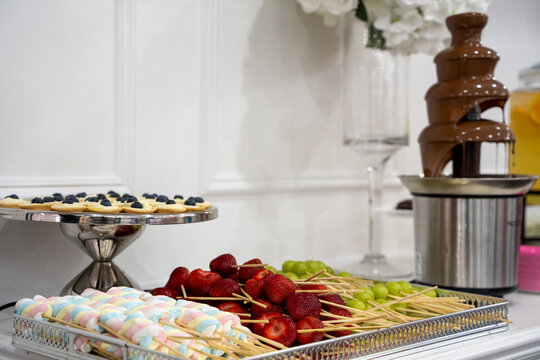 View of chocolate fountain with fruit and marshmallow skewers.