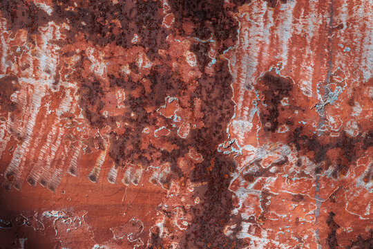 Red textured background with rust and paint cracks. Peeling blue paint, a reddish-brown base. Raised patches of paint. The aged surface of the steel sheet. Natural shadows