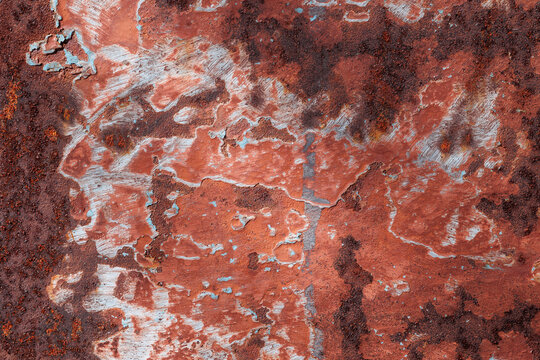 Red textured background with rust and paint cracks. Peeling blue paint, a reddish-brown base. Raised patches of paint. The aged surface of the steel sheet. Natural shadows