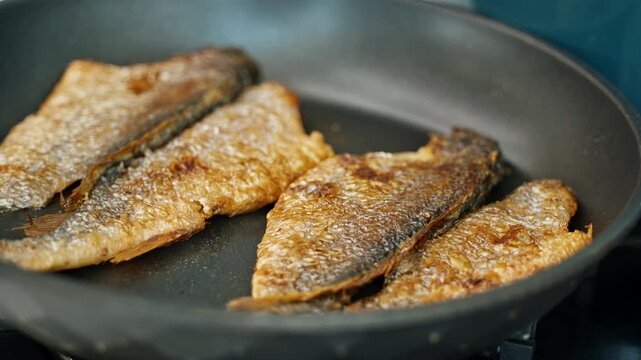 A close-up of golden crispy grilled or pan-fried fish fillets in a cooking pan in a bright kitchen setting.