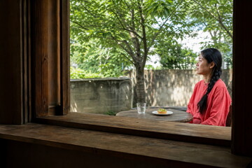 Fototapeta premium 緑の庭を望む木の窓辺でピスタチオタルトを前に座る一人の女性