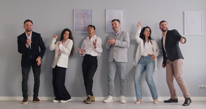 Young funny business people and company employees in formal suits dancing having fun and celebrate their success in business or making a deal standing indoors. Teamwork concept. 4k video
