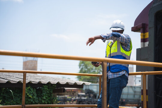 Tired construction worker wiping sweat under the hot sun, Railway worker in hard hat and safety vest on train platform, Technician checking train equipment at the railway station
