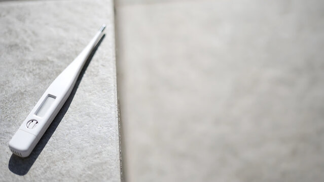 A digital medical thermometer lying on a textured gray background for healthcare concept