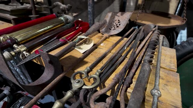 Collection of old rusty metal fireplace tools and farm equipment on a wooden table in a workshop
