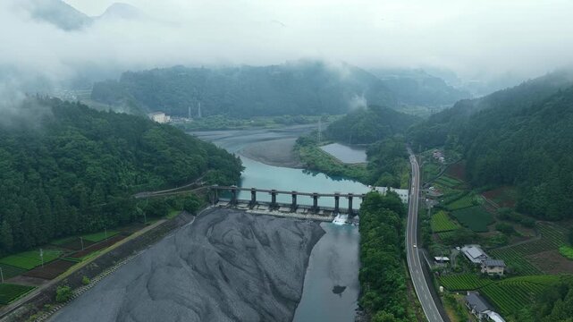 Aerial drone footage of weir dam and river valley in misty mountains, Shizuoka, Japan