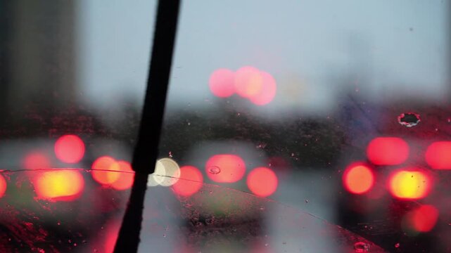 A car driving on a rainy night, with blurred city lights visible through the windshield, as the wipers clear the raindrops