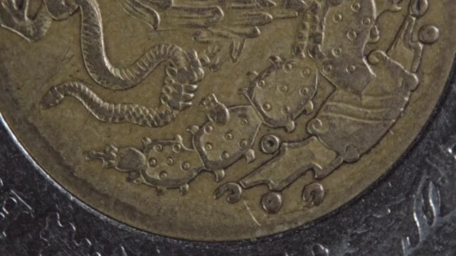 Macro view of eagle and snake engraving on coin surface, highlighting raised relief details, metallic texture, and symbolic design elements in close perspective.