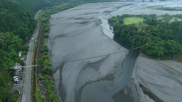 Aerial drone footage of Oi River wide gravel riverbed and suspension bridge in Shizuoka, Japan