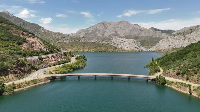 Drone view of a small road bridge crossing a blue mountain reservoir
