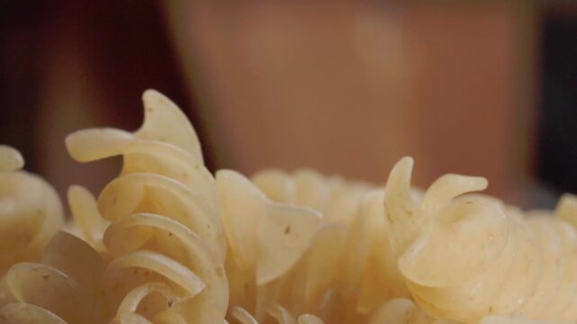 Macro close up of dry spiral pasta highlighting curled shape, smooth texture and natural color. Detailed food footage showcasing uncooked noodles, culinary ingredient and cooking preparation